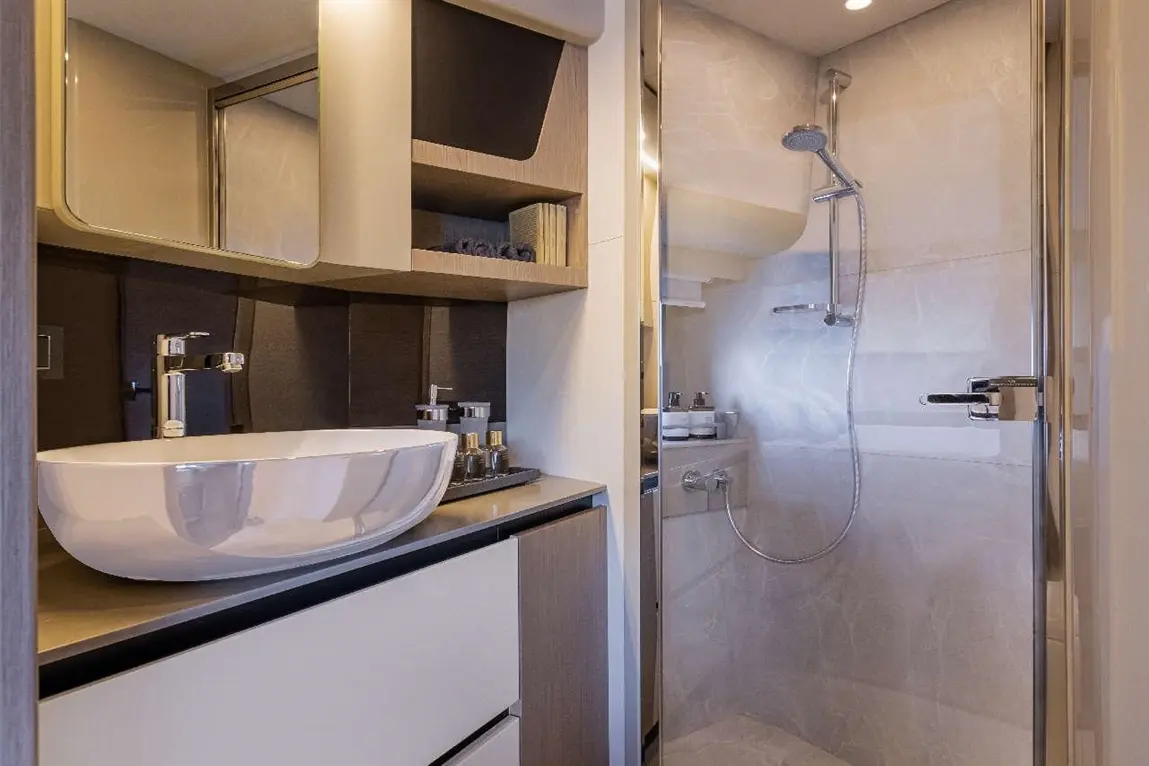 A modern bathroom featuring a stylish basin, sleek shower, and organised shelving with toiletries and a large mirror.